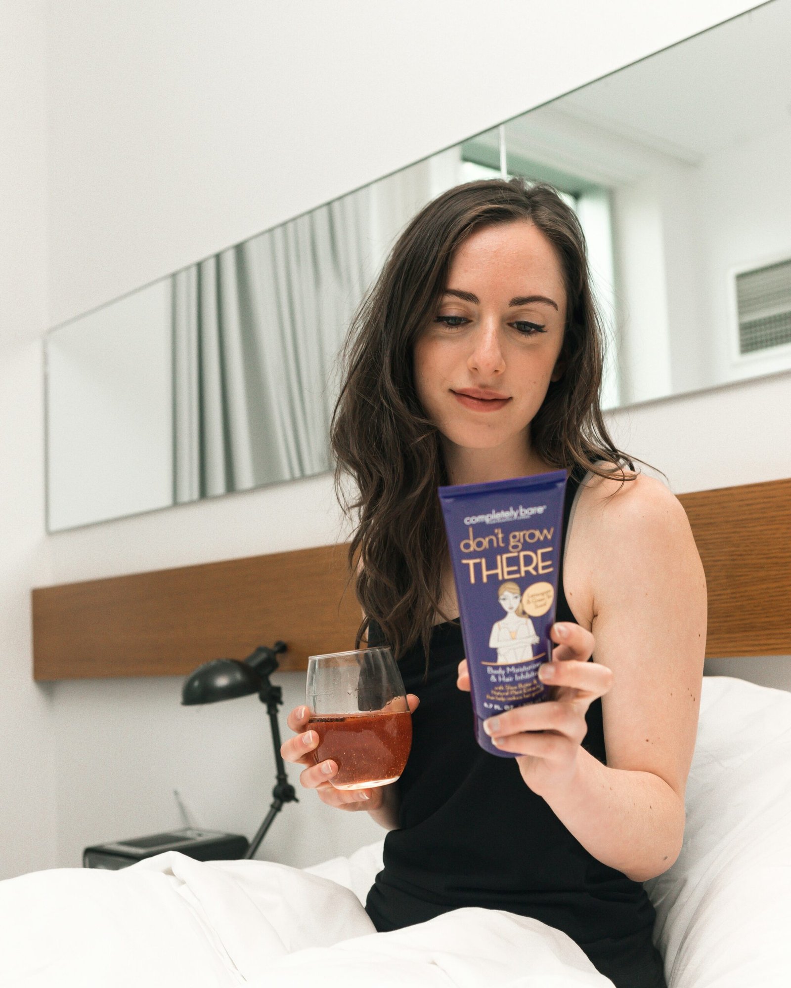 a woman sitting on a bed holding a drink and a book